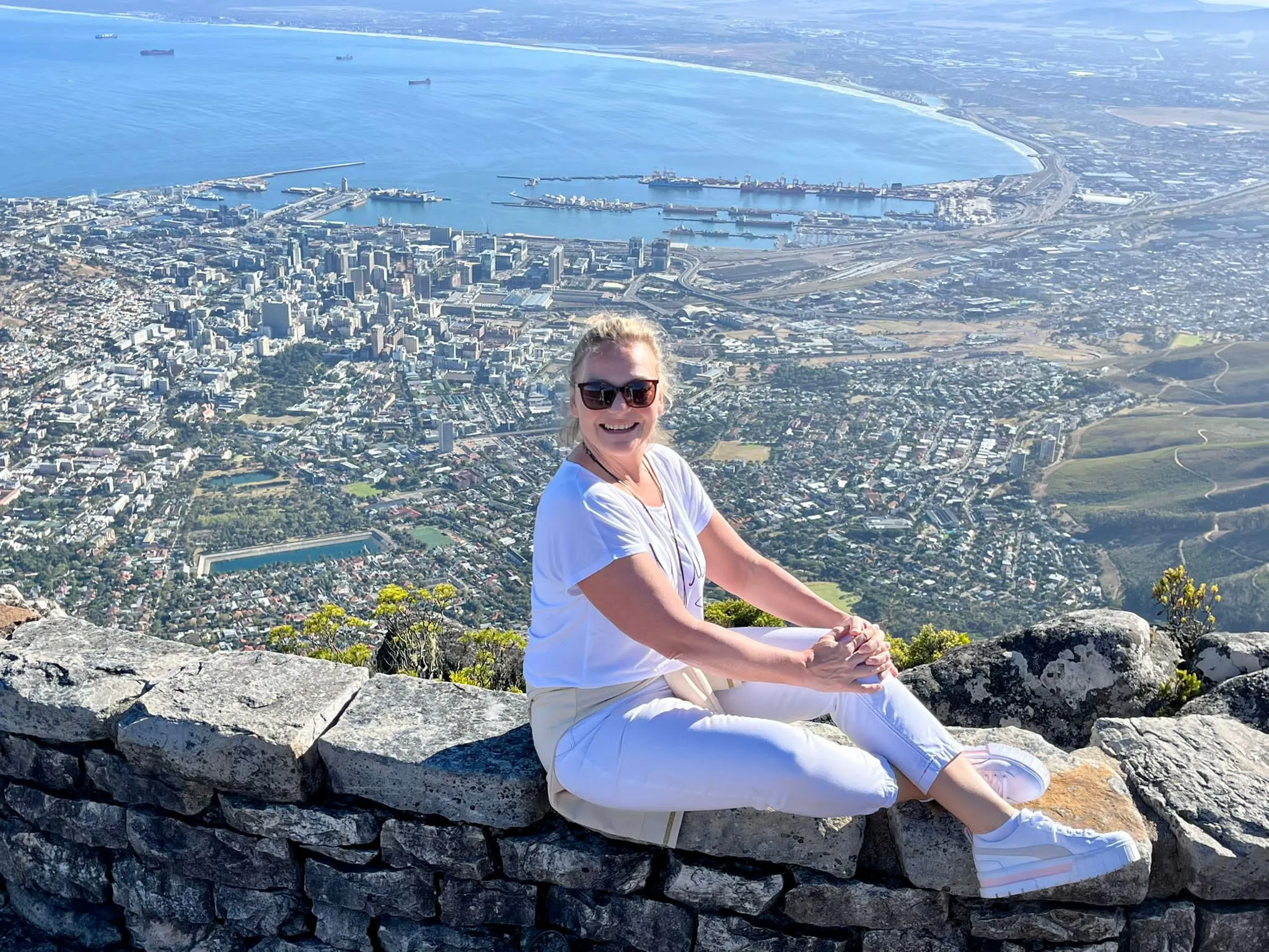 Frau sitzt auf einer Mauer mit großer Stadt und Hafen im Hintergrund