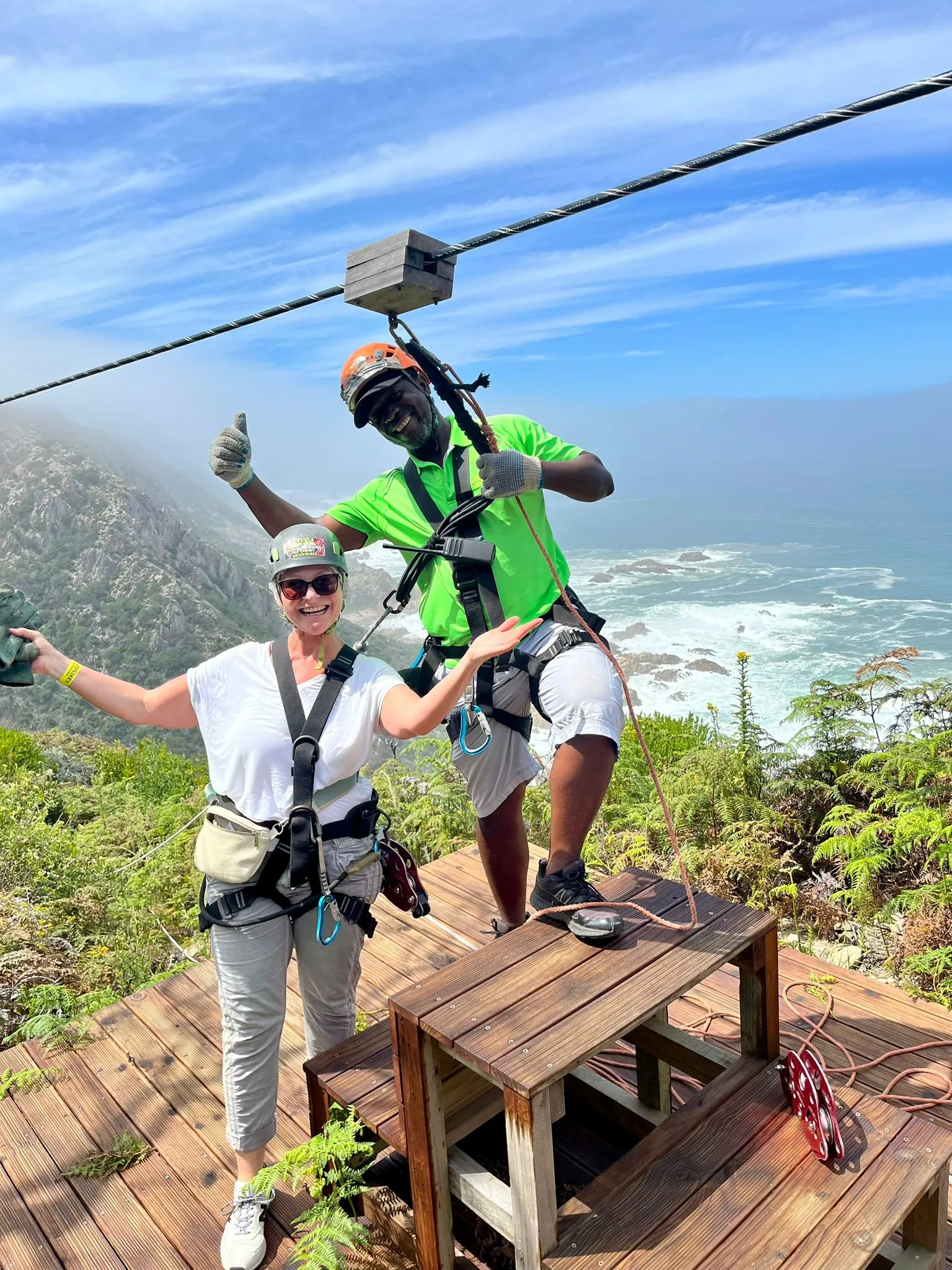 Frau steht mit einem Guide auf einem Berg an einer Zipline