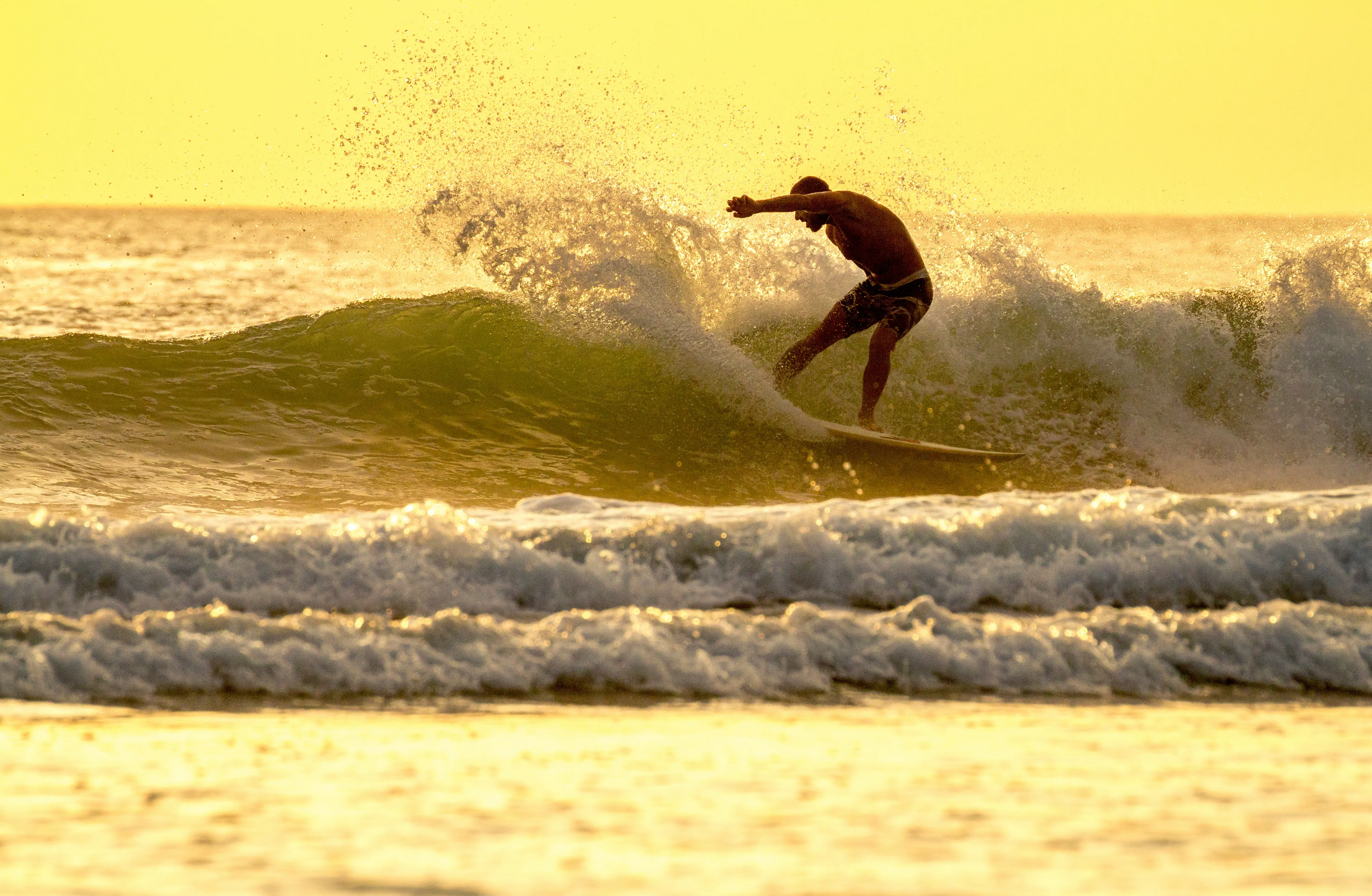 Surfer auf einem Surfbrett, der eine Welle bei Sonnenuntergang reitet.