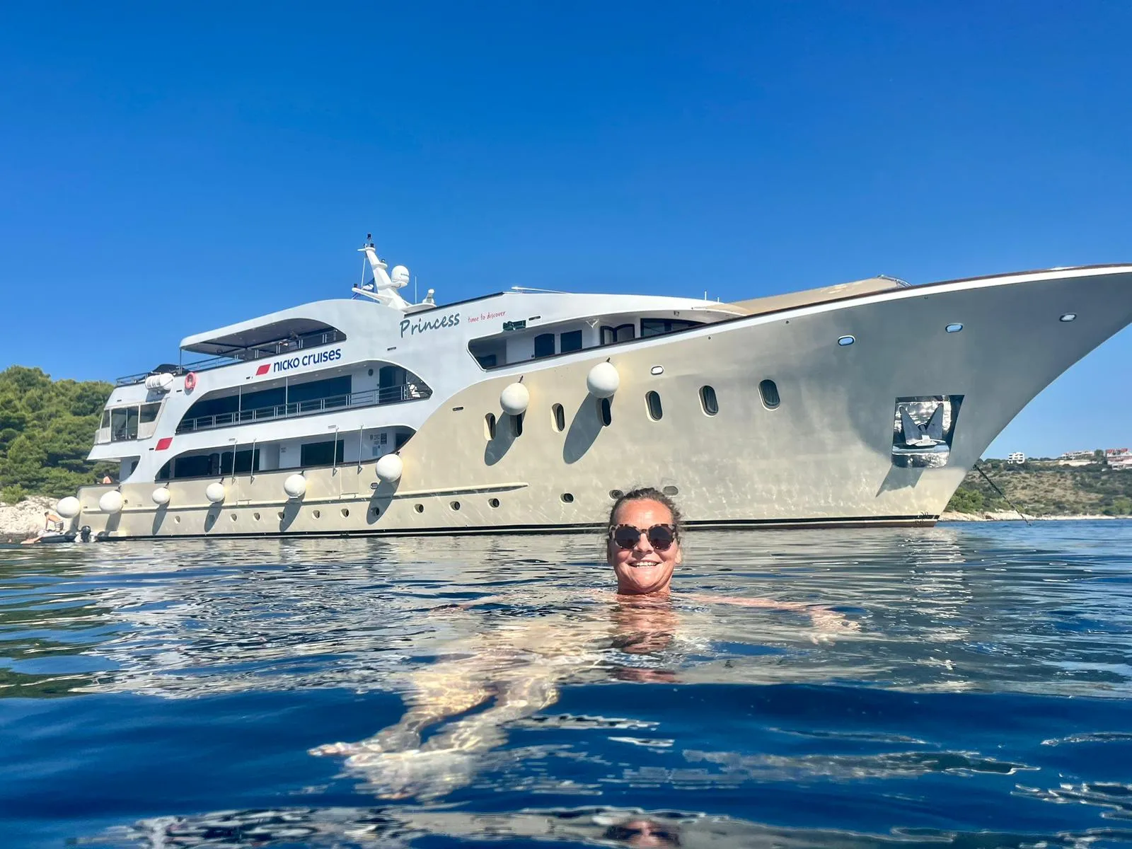 Große weiße Yacht mit der Aufschrift 'Princess' und 'nicko cruises' liegt auf ruhigem Wasser, im Vordergrund schwimmt eine Person.