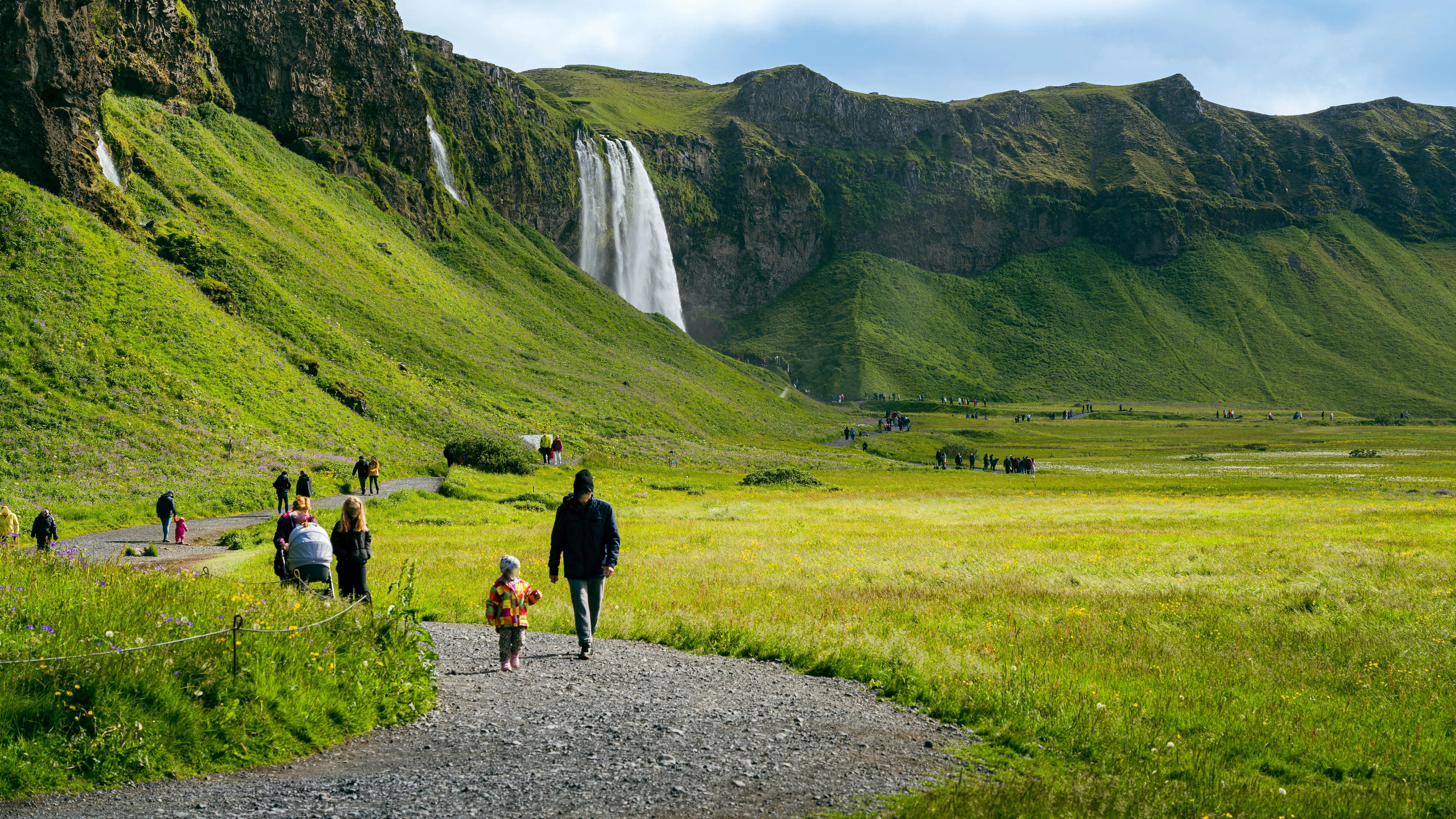Familien sind auf flachem Weg am Wandern mit einem Wasserfall im Hintergrund
