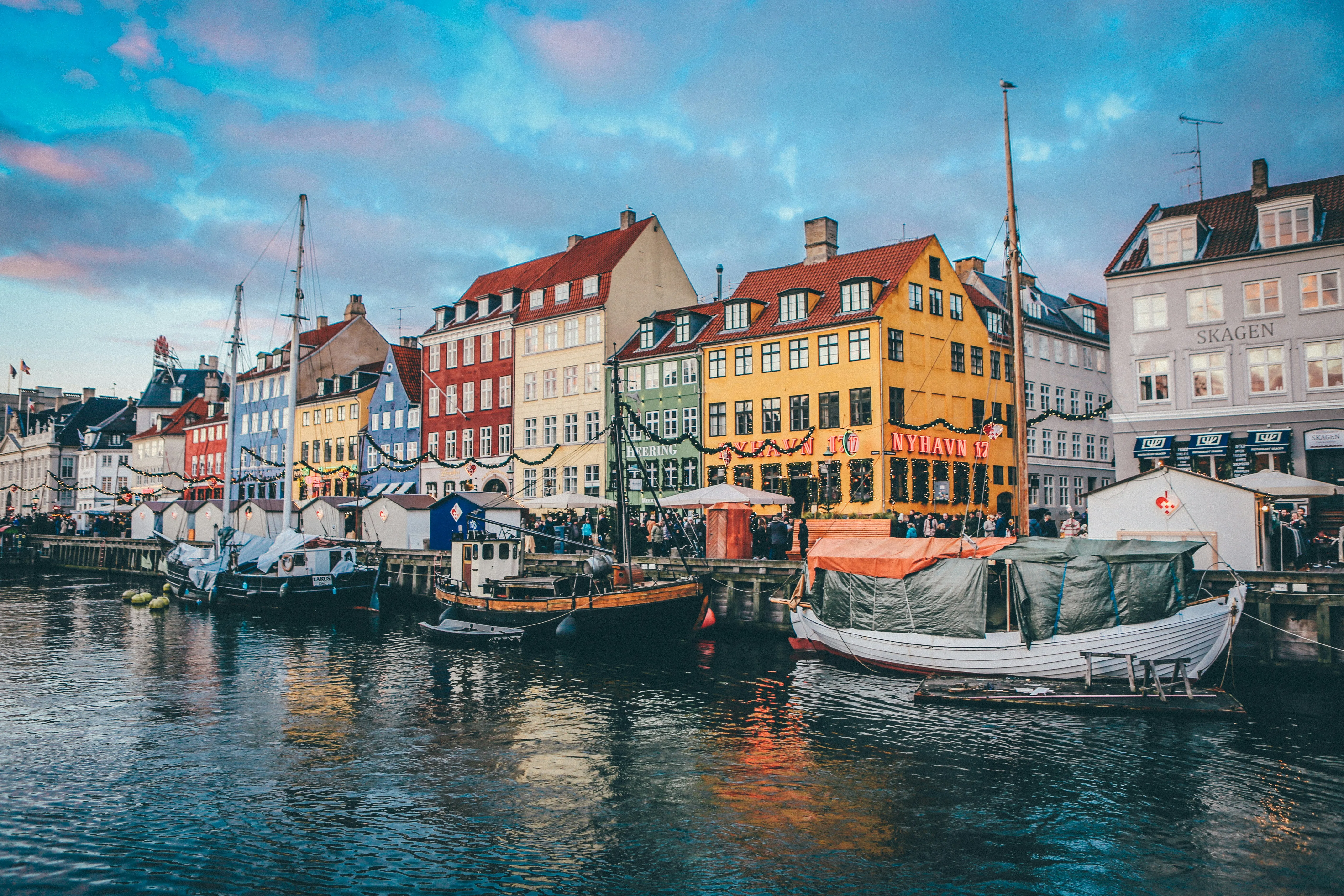 Bunte mehrstöckige Häuser am Wasser mit mehreren Segelbooten im Hafen unter blauem Himmel.