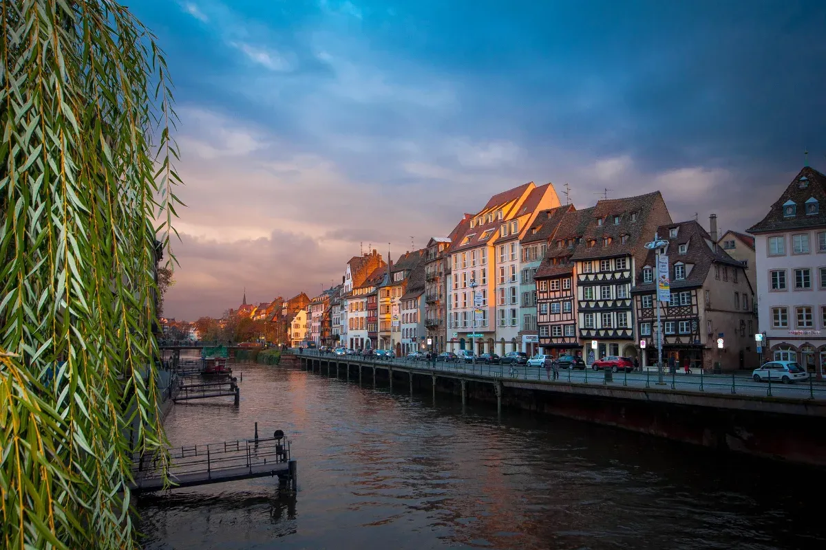 Flussufer mit historischen Fachwerkhäusern und Bäumen bei Sonnenuntergang in einer Stadt