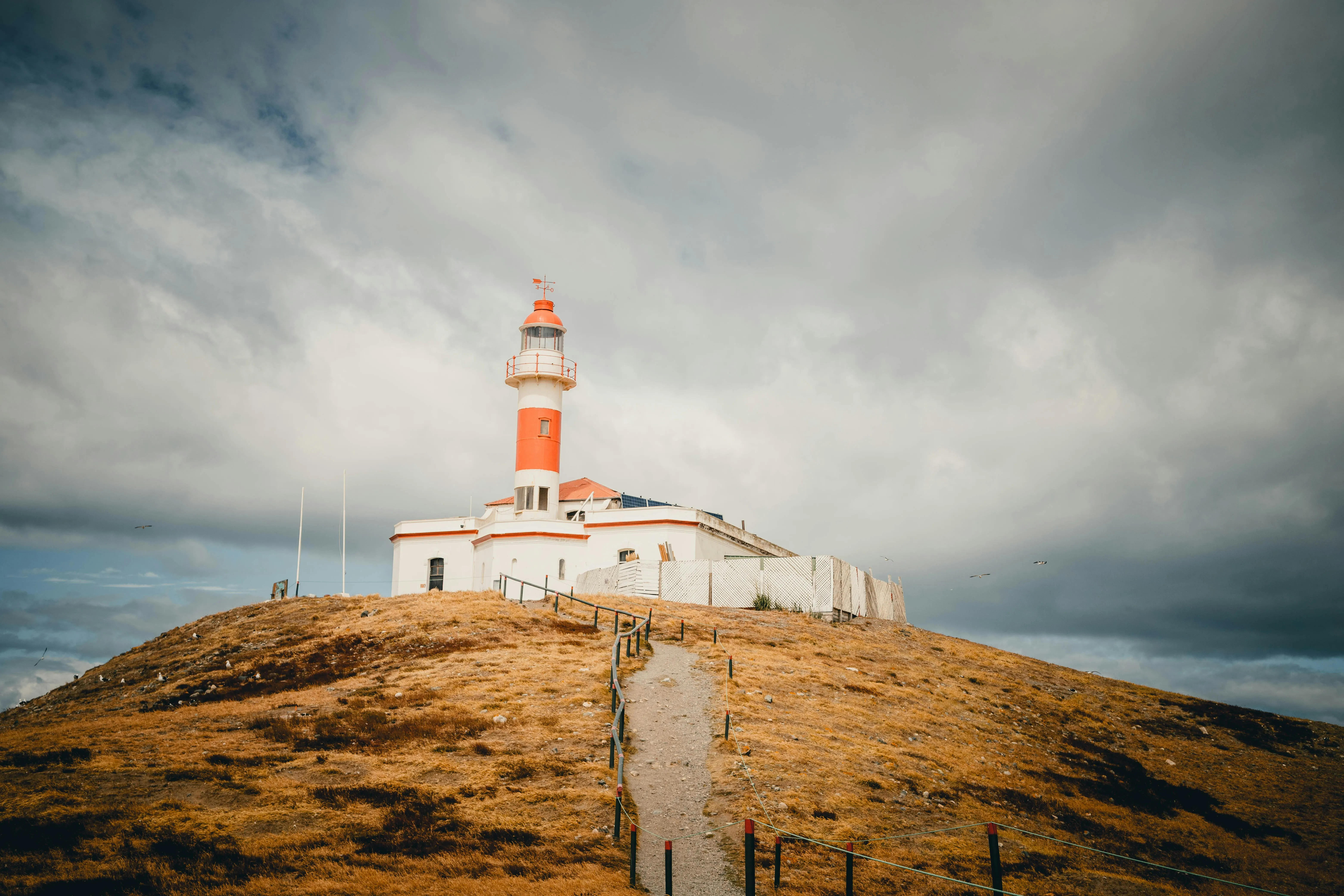 Leuchtturm auf einem kahlen Hügel mit einem schmalen Weg, der zum Gebäude führt, unter bewölktem Himmel.