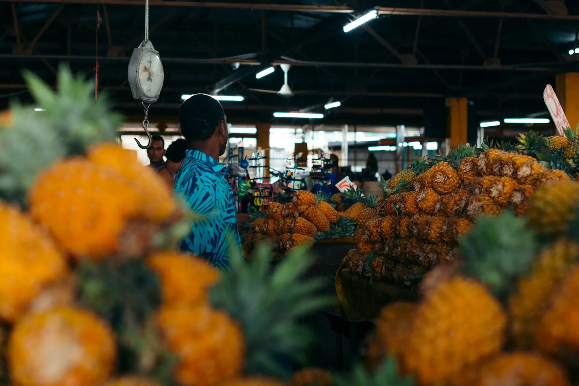 Markthalle mit mehreren großen Stapeln von Ananas und einer Person in blauem Hemd, die an einer Waage steht.