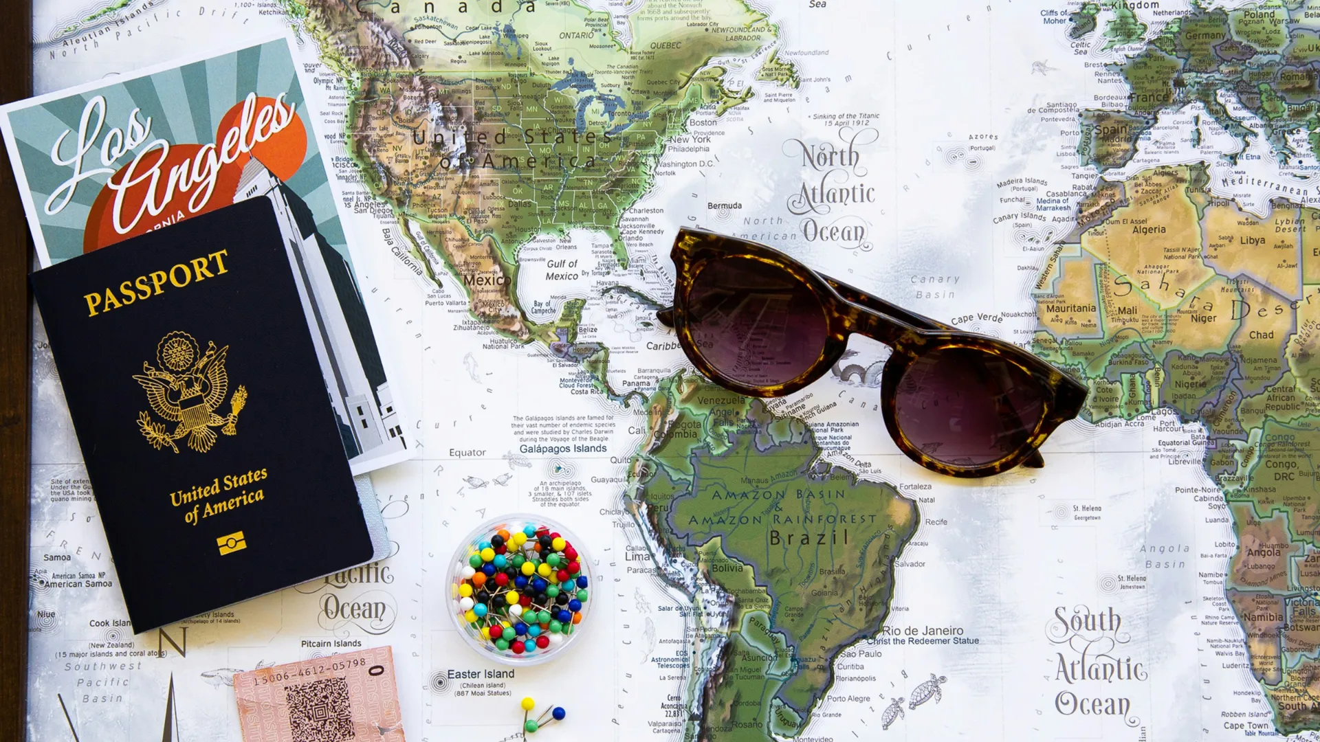 Weltkarte mit Sonnenbrille, US-Pass, Los-Angeles-Reiseführer, bunten Perlen und Fahrkarte.