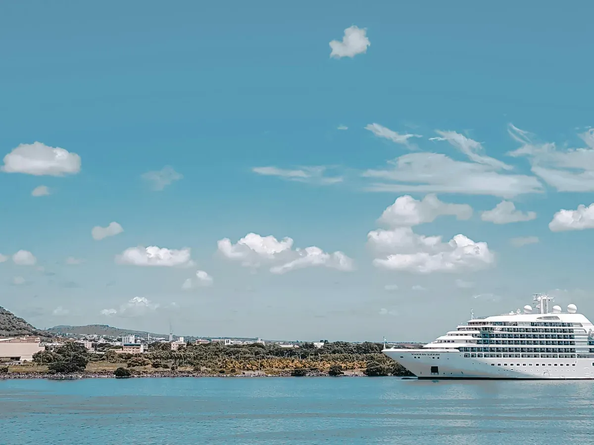 Kleines Kreuzfahrtschiff vor einer Küste, im Hintergrund Berge und eine Stadt