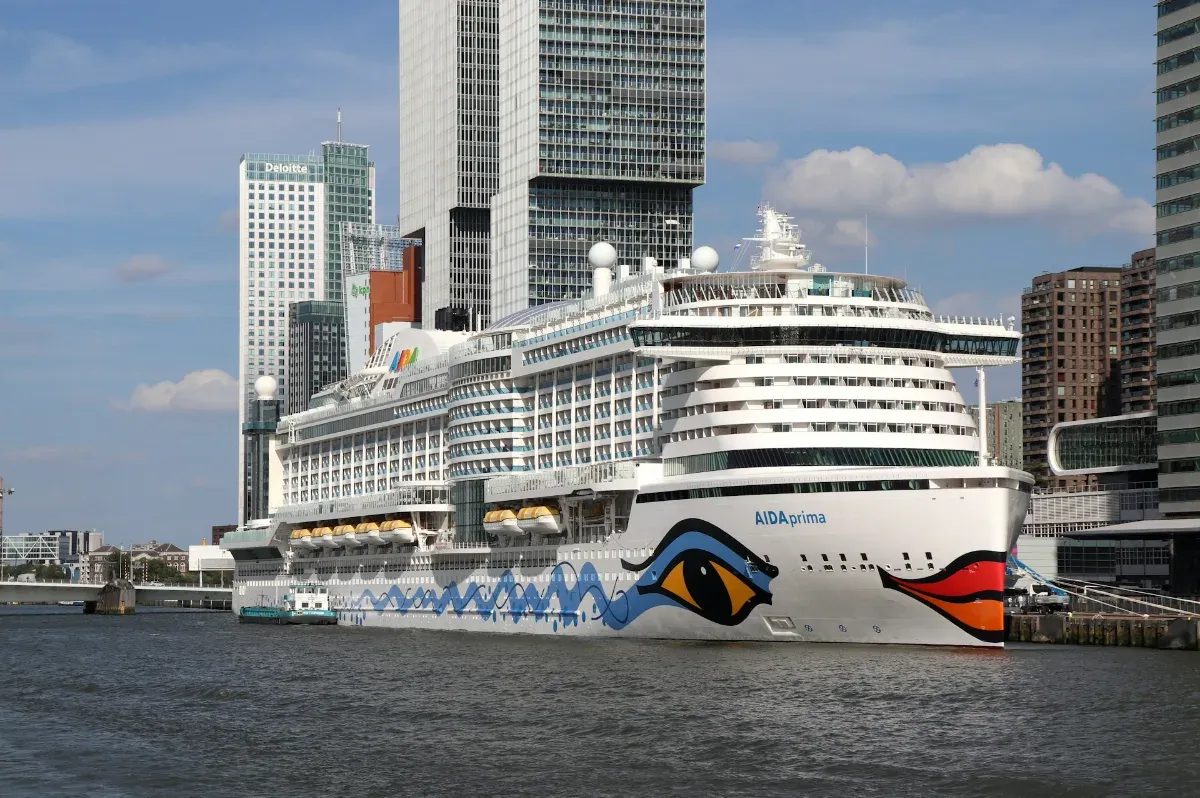 Großes Kreuzfahrtschiff mit markanter Augen- und Lippenbemalung am Bug vor einer Stadt mit Hochhäusern