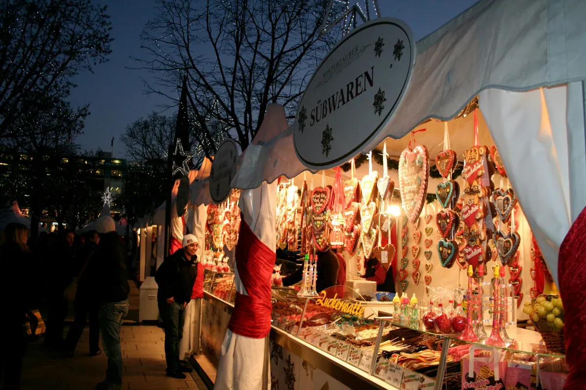 Weihnachtsmarktstand mit Lebkuchenherzen und Süßigkeiten bei Dämmerung