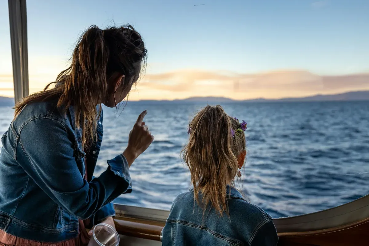 Zwei Personen mit Pferdeschwanz und Jeansjacken blicken aus einem Bootsfenster auf das Meer
