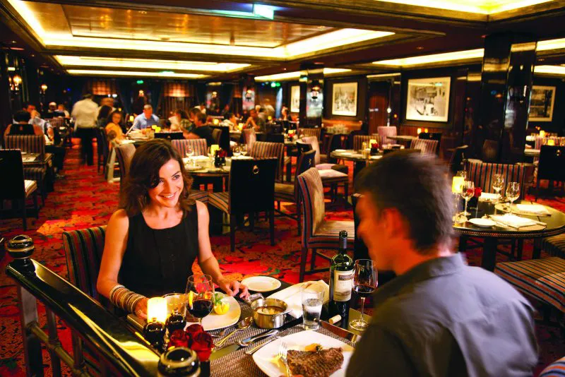 Zwei Personen sitzen an einem gedeckten Tisch in einem eleganten Restaurant mit gedämpfter Beleuchtung und roten Teppichböden