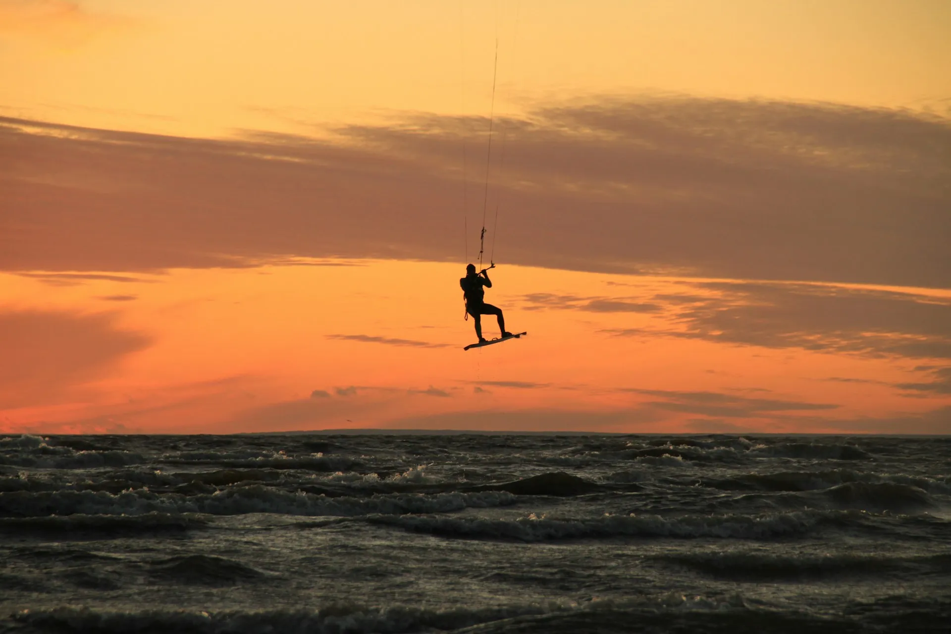 Silhouette einer Person beim Kitesurfen über dem Meer vor orangefarbenem Sonnenuntergangshimmel