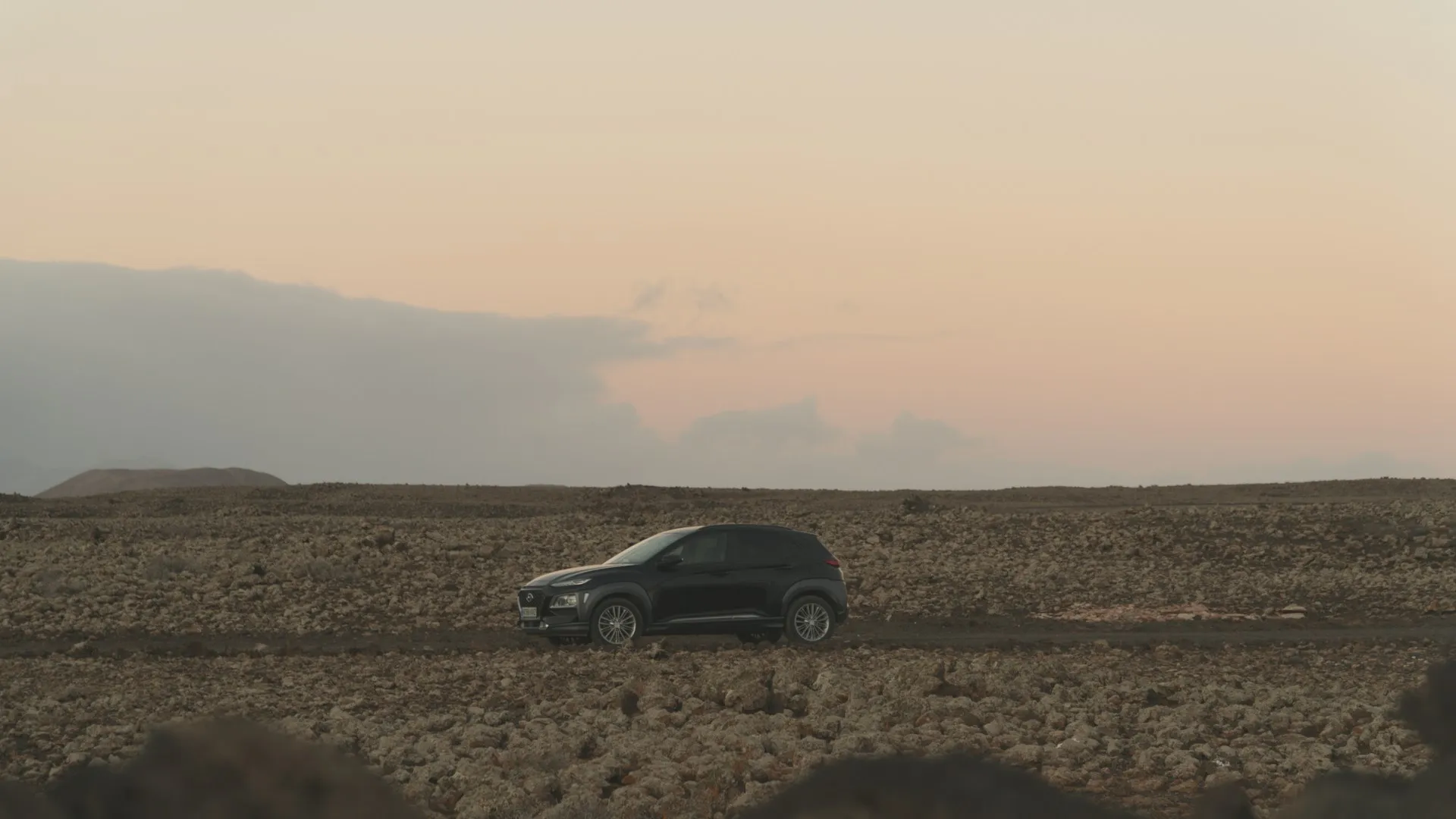 Geländewagen fährt auf unebenem, felsigem Terrain unter bewölktem Himmel