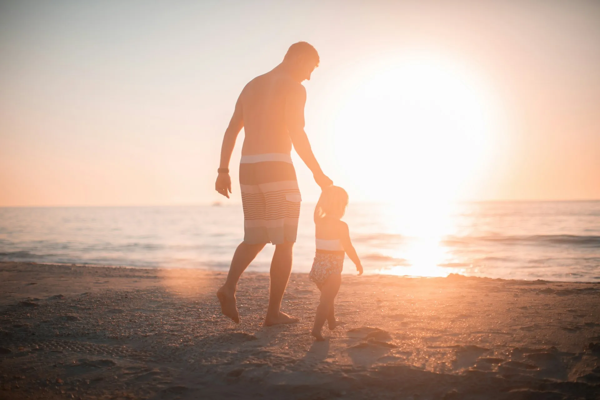 Ein Mann und ein Kleinkind laufen am Strand bei Sonnenuntergang Hand in Hand