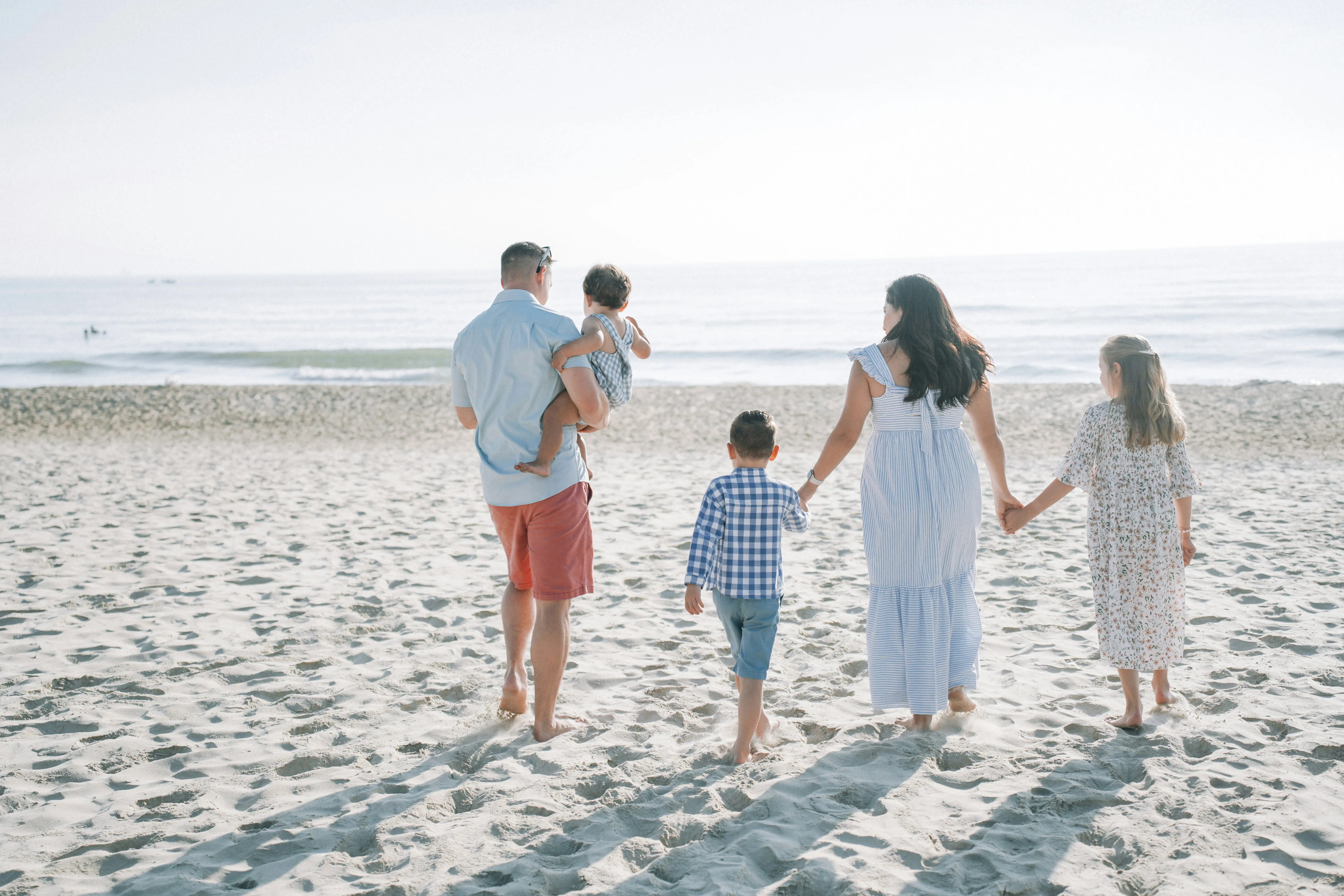 Familie mit drei Kindern von hinten auf einem weißen Sandstrand