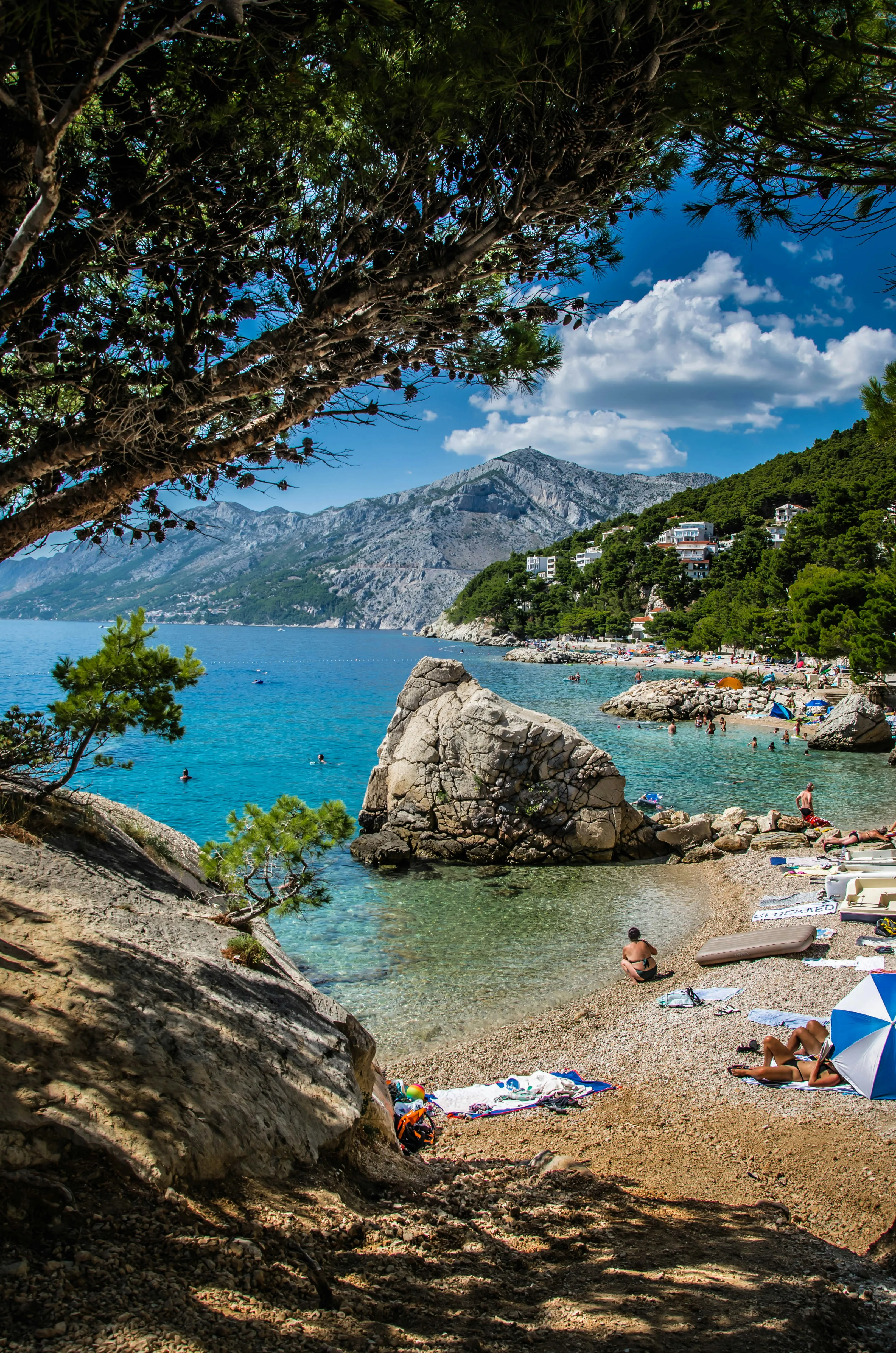Blick aus einer Bucht mit entspannenden Urlaubern und Bergen im Hintergrund