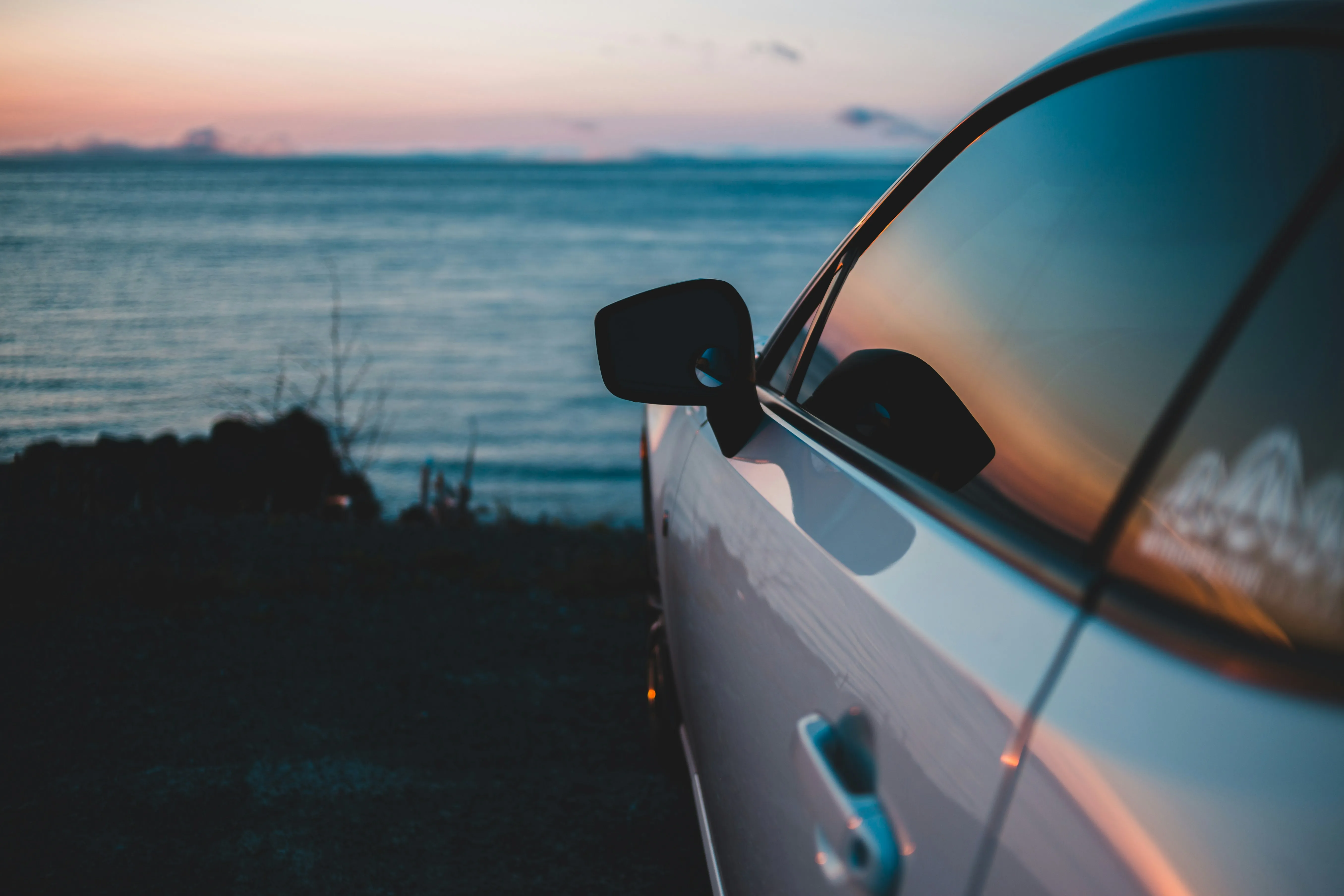 Auto steht an einer Küste beim Sonnenuntergang