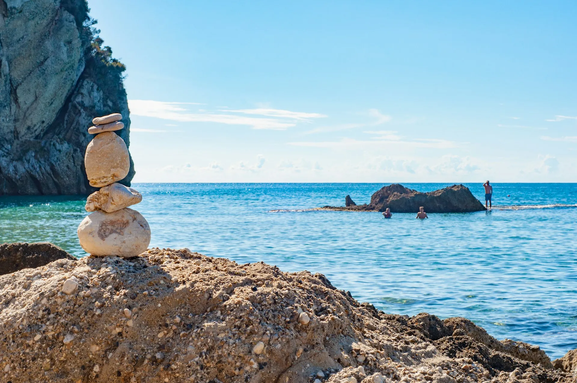 Steinmännchen auf Felsen am Meer mit Menschen und Felsen im Wasser im Hintergrund