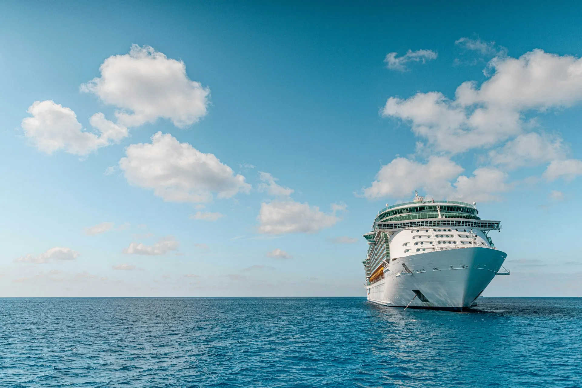 Blick von einem Schiff mit Liegestühlen auf das Meer und eine hügelige Küstenlandschaft unter blauem Himmel mit Wolken