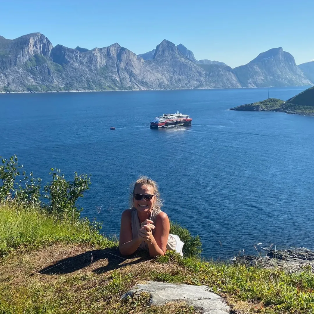 Frau auf dem Berg vor einem Kreuzfahrtschiff, dass auf See liegt