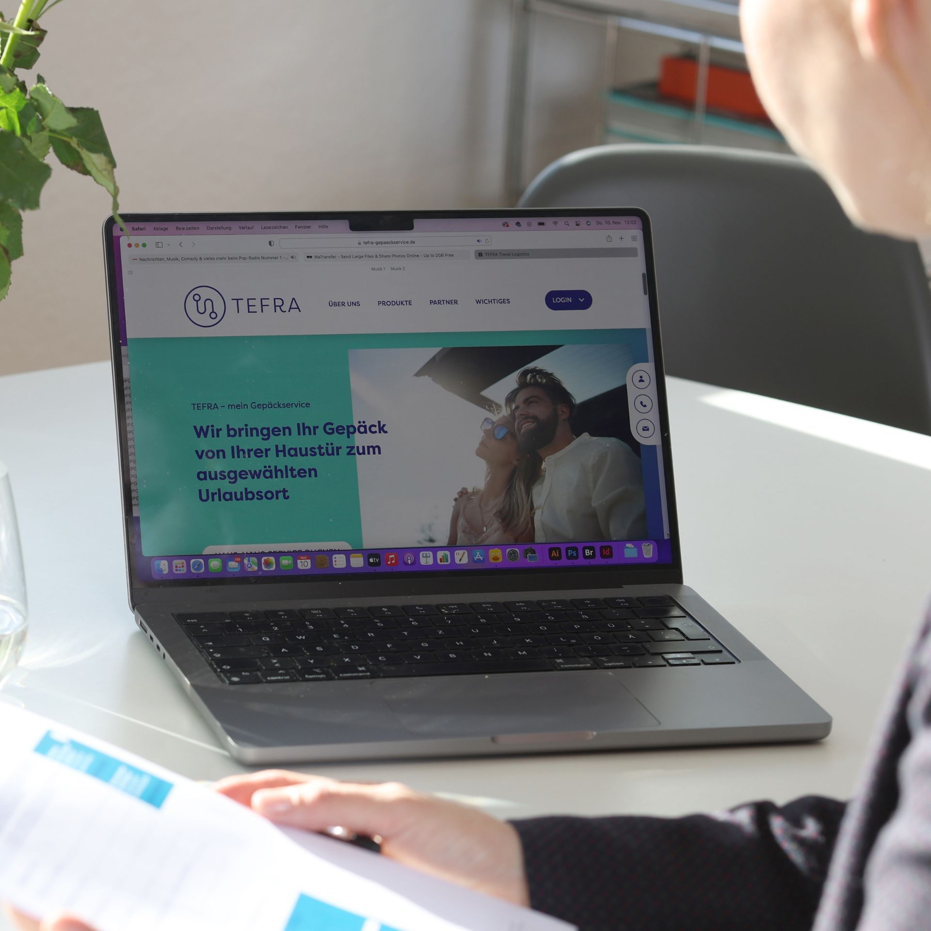 Laptop mit geöffneter Webseite von TEFRA Gepäckservice auf einem weißen Tisch, im Vordergrund eine Person mit Dokumenten in der Hand