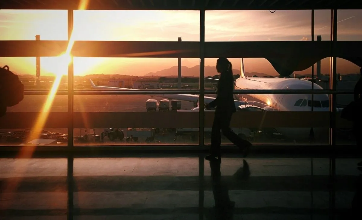 Silhouette einer Person, die in einem Flughafen-Terminal vor großen Fenstern mit Blick auf ein Flugzeug und den Sonnenuntergang geht